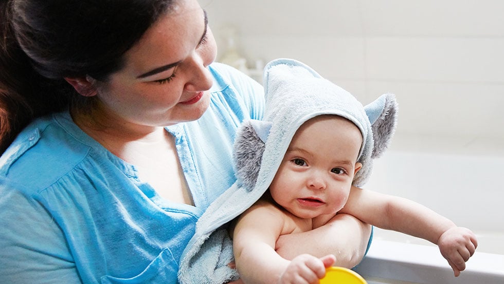 Mother cuddling her baby and drying him off after a bath