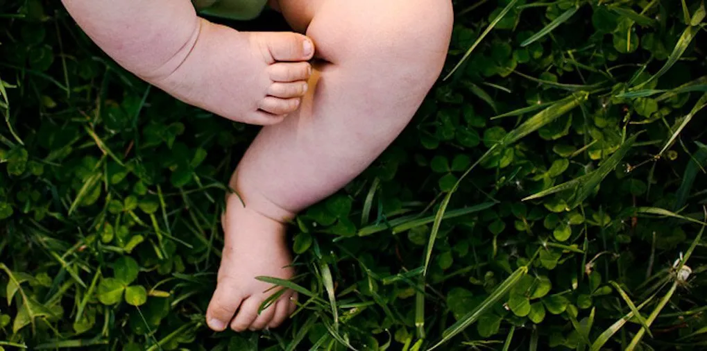 Close-up of a baby's feet resting on green grass, emphasizing gentle and natural elements.