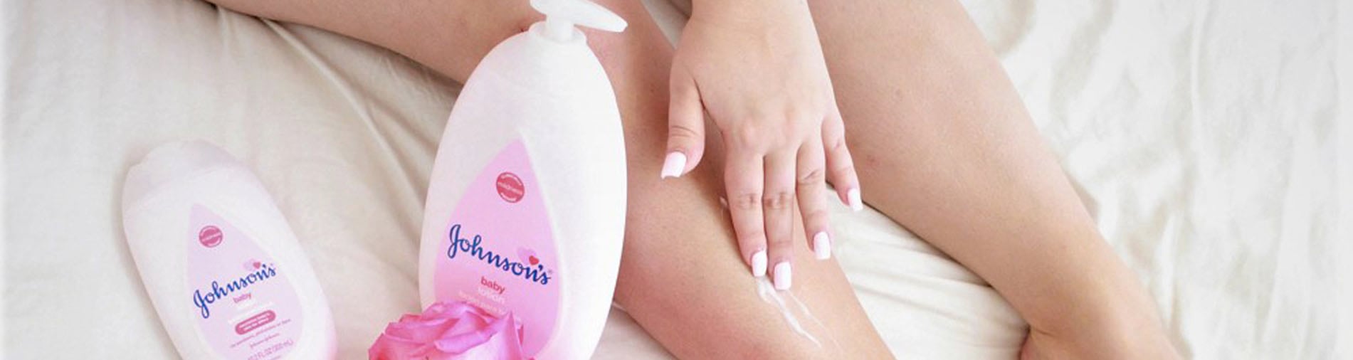 Johnson's Baby lotion bottles next to a person applying lotion on their leg with a pink rose in the background.