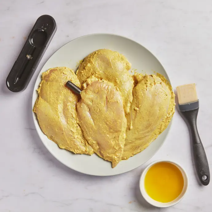 A picture of marinated chicken breasts with olive oil and the Yummly Smart Thermometer, ready to be grilled