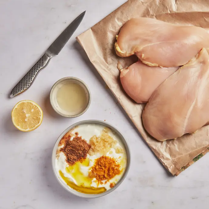A picture of chicken breasts and ingredients for a marinade, including lemon juice, yogurt, and Indian spices