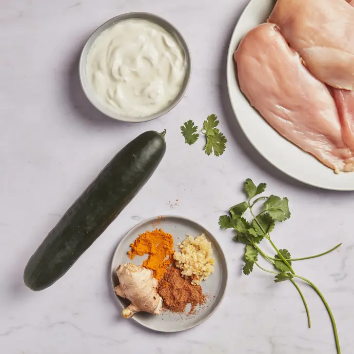 A picture of ingredients to make Indian Spiced Grilled Chicken Breasts with Creamy Raita, including yogurt, chicken, cilantro, spices, and cucumber