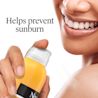 Smiling woman holding Neutrogena® sunscreen bottle, helps prevent sunburn with daily protection
