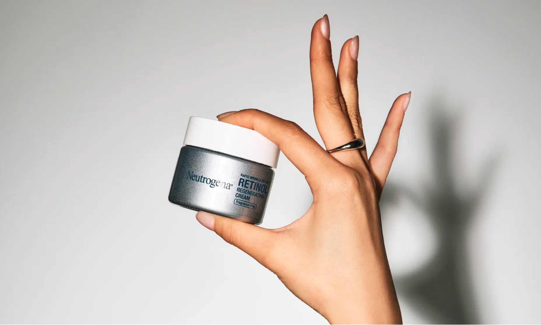 Woman's hand with youthful skin holding up a jar of Neutrogena® Rapid Wrinkle Repair® Retinol Regenerating Cream Fragrance Free