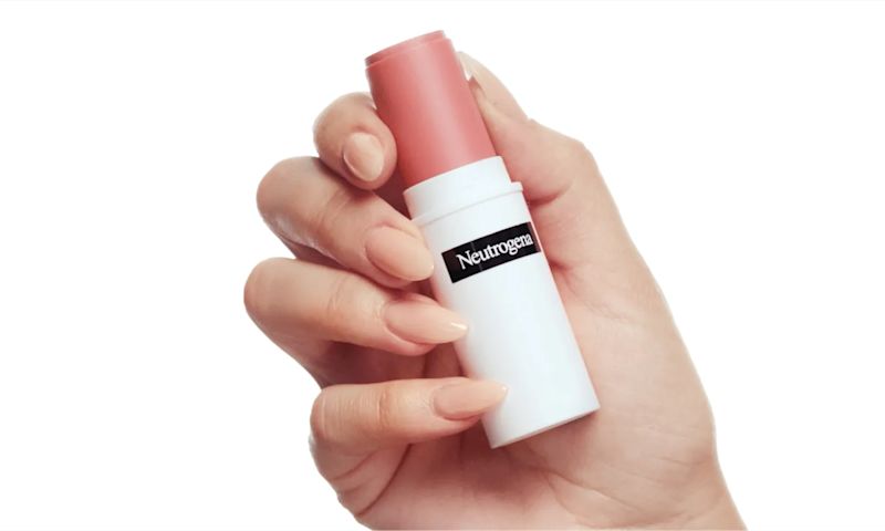 A woman holding a stick of Neutrogena® Healthy Glow Blush Stick Spiced Rose in her hand