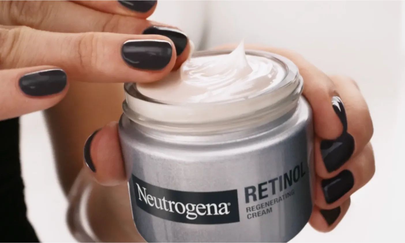 Hand with painted nails holding a jar of Neutrogena® Rapid Wrinkle Repair® Fragranced Retinol Regenerating Cream