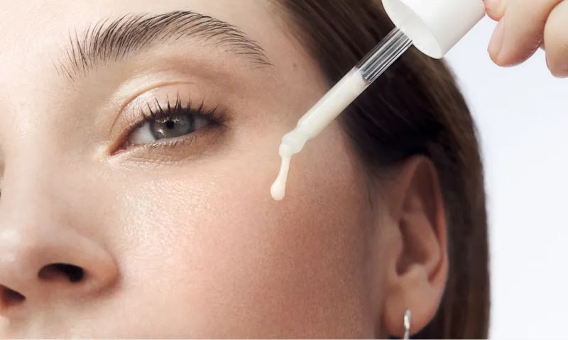 Woman with healthy skin applying dropper full of Rapid Wrinkle Repair® Serum to face