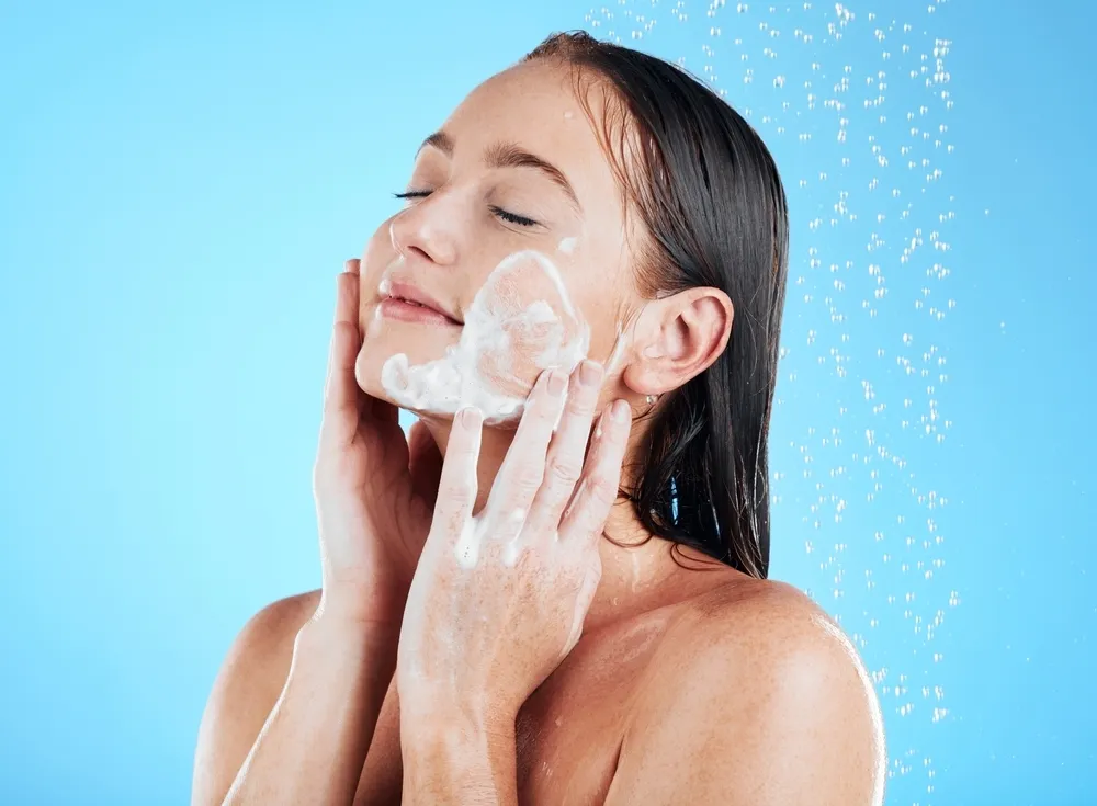 woman washing face with soap on blue background for grooming, cleaning and wellness.