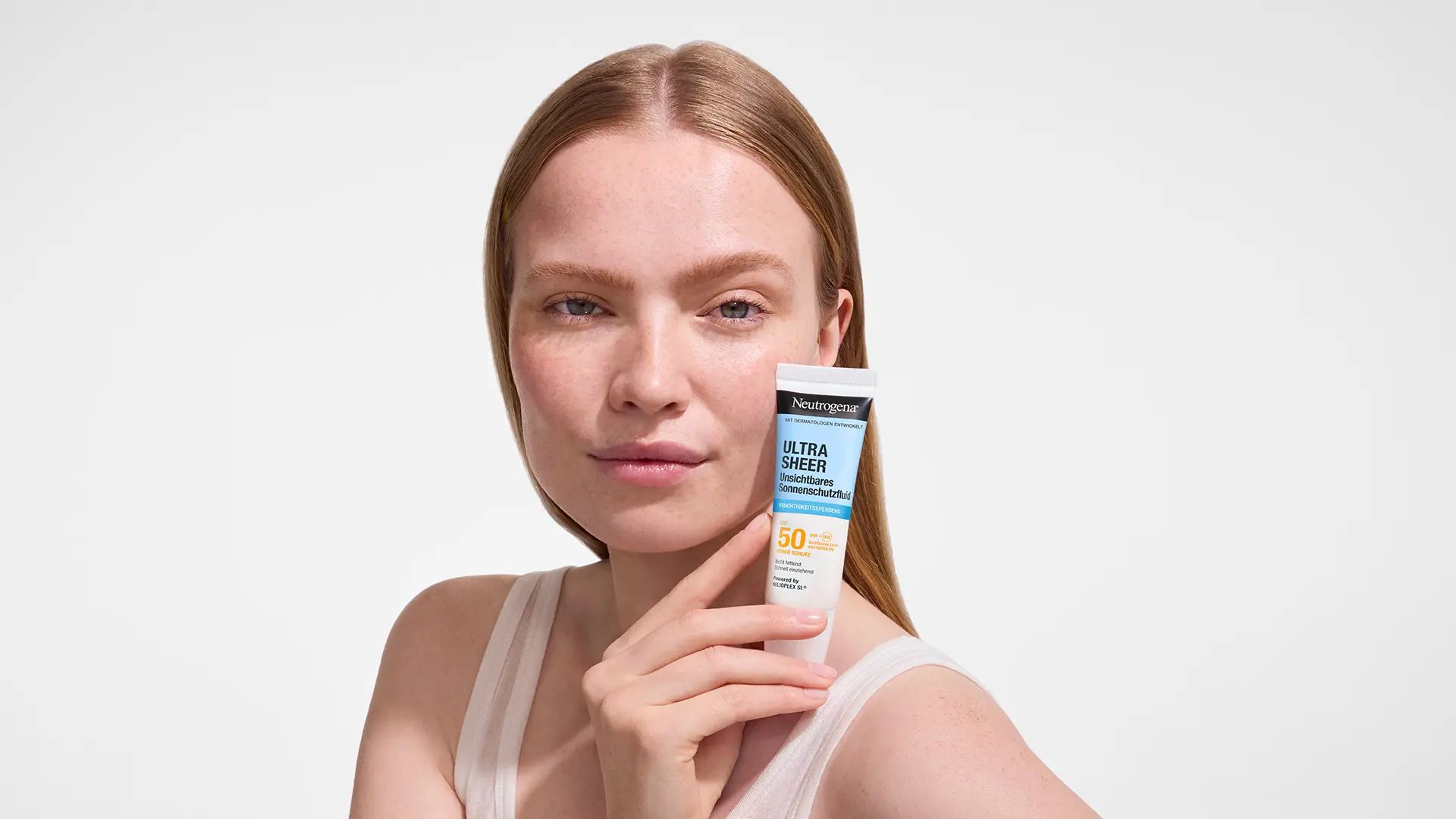 Engla Erikson hält eine Tube Ultra Sheer unsichtbares Sonnenschutzfluid nah an ihrem Gesicht