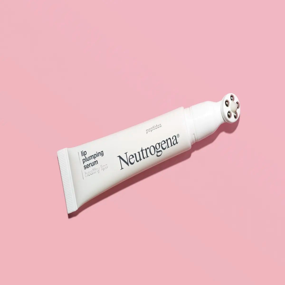 A tube of Neutrogena® Lip Plumping Serum applicator set against a solid pink background.