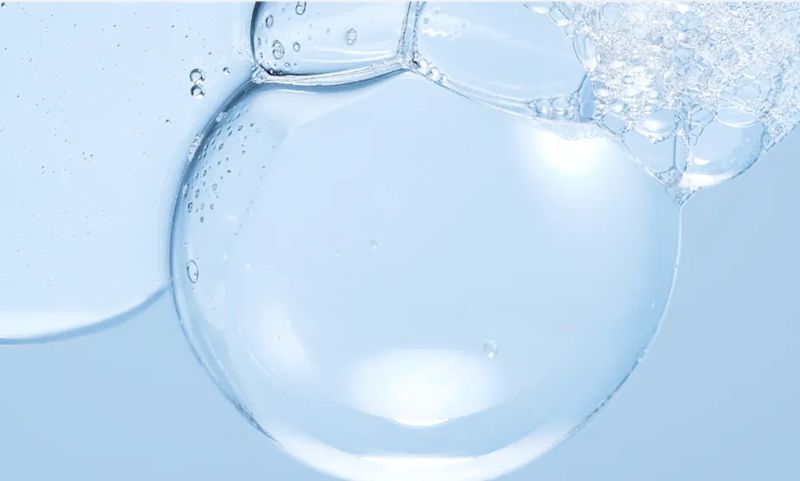 Close-up of a large, translucent water bubble surrounded by a cluster of smaller foam bubbles against a light blue background.