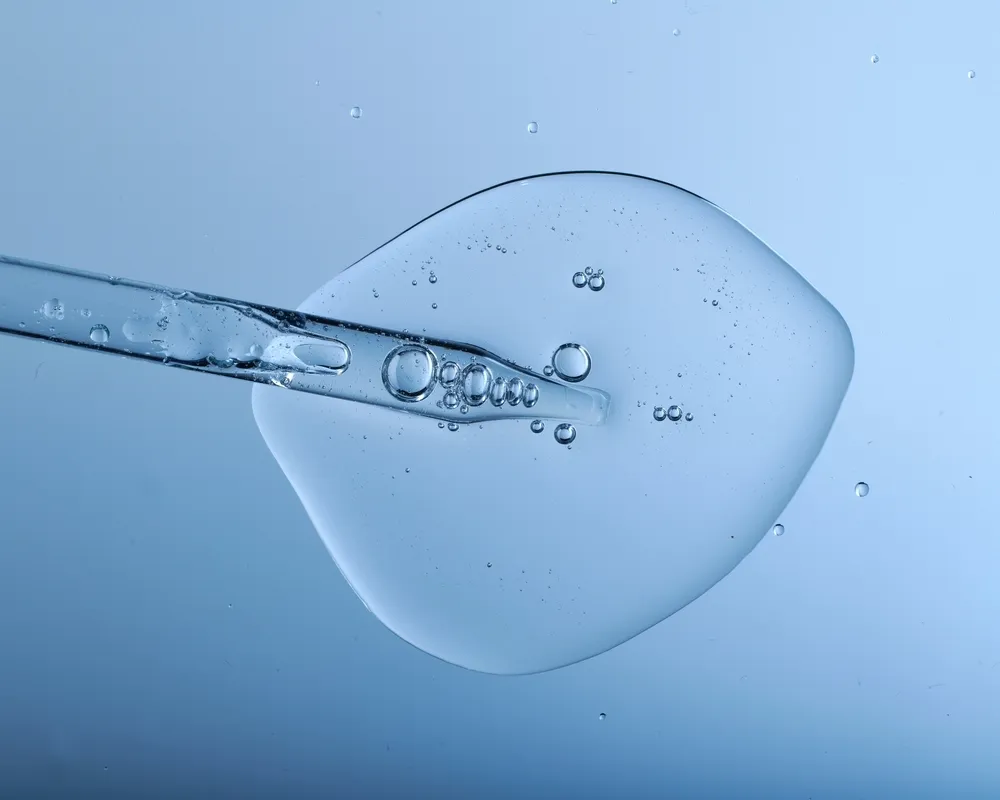 Pipette with bubbles and clear formulation being expelled. Clear liquid with bubbles resembling glycerin, hyaluronic acid or keratin in laboratory or scientific setting.