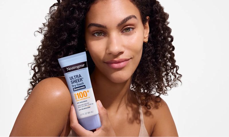 woman smiling holding Neutrogena Ultra Sheer Dry-Touch Broad Spectrum Max SPF 100+ Body Sunscreen, 3 Oz