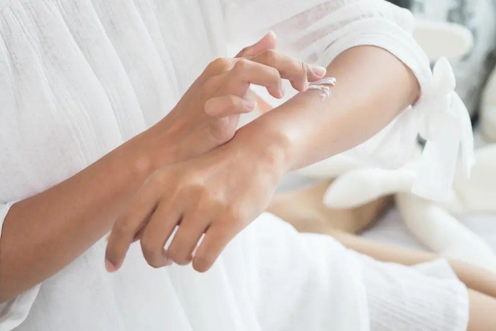 Eine junge Frau cremt sich den Arm mit einer Hautcreme ein.
