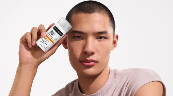 A Man with clear skin holding a bottle of Neutrogena® Cloud Tech™ Clear Face Sunscreen for Acne Prone Skin