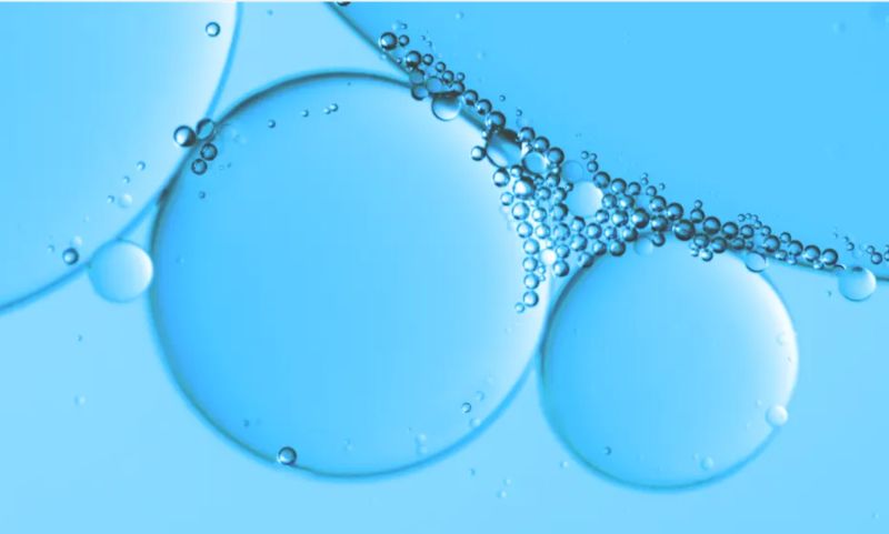Close-up of clear, blue liquid containing large, translucent bubbles and numerous smaller bubbles clustered together.