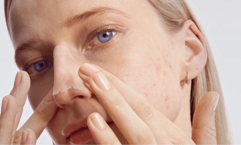 Young woman applying Neutrogena nose patch strip to reduce blemishes.