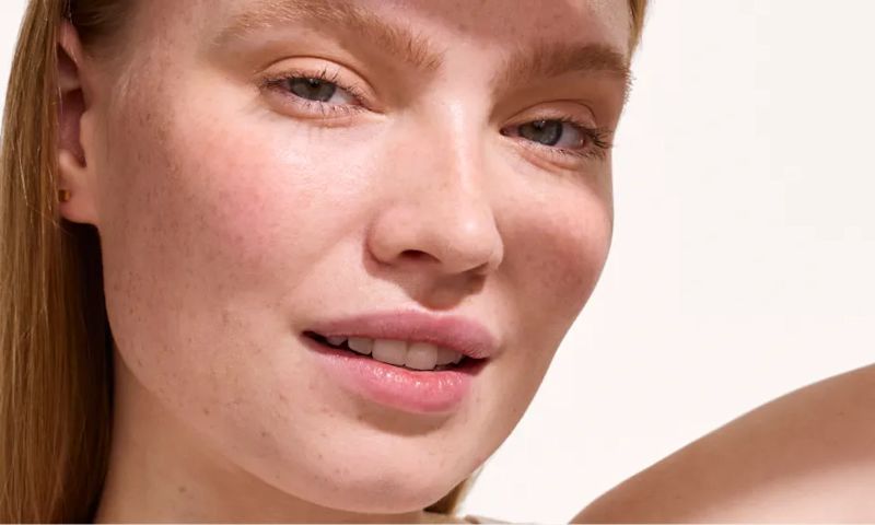 Close-up portrait of a woman with light freckles and natural makeup, looking at the camera.