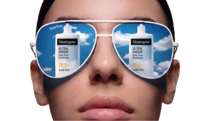 Woman wearing sunglasses reflecting the sky packaging of Neutrogena® Cloud Tech™ Bemotrinzinol BEMT sunscreen