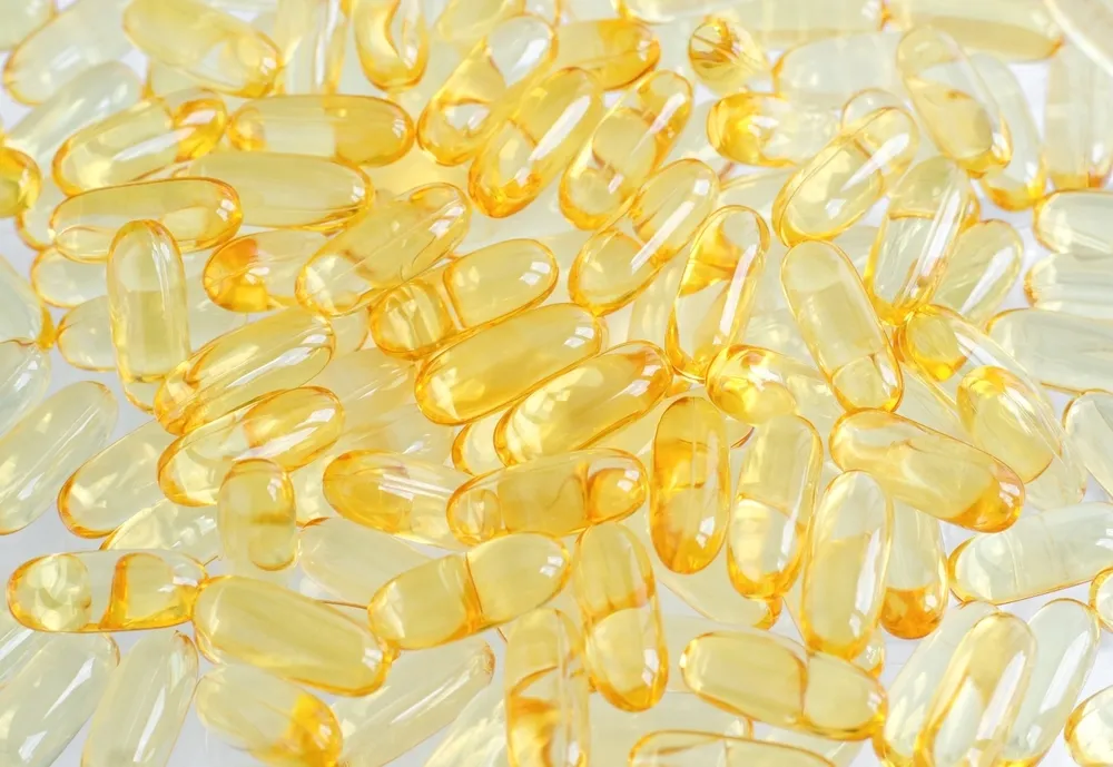 A smiling woman holds up a gel capsule filled with yellow liquid.