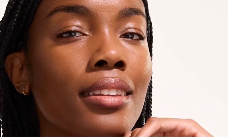 Close-up portrait of a woman with braided hair and smooth skin, gently touching her chin.