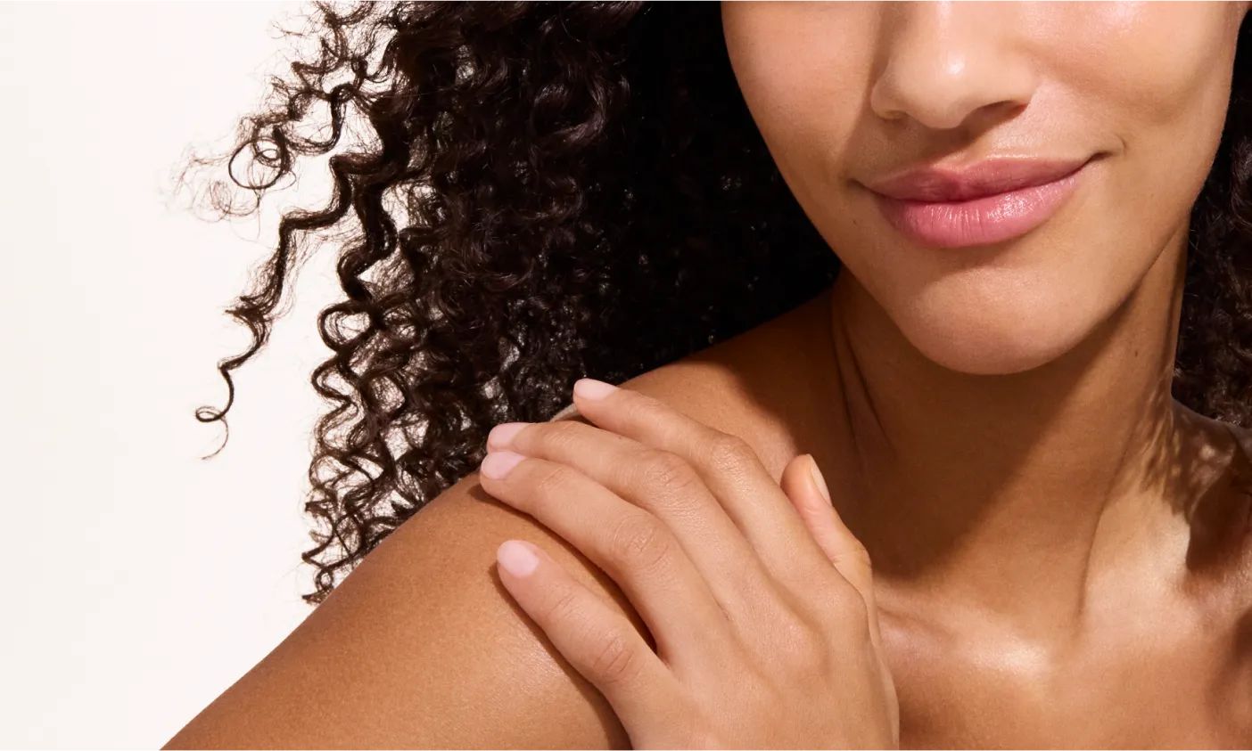 Woman with curly hair applying Neutrogena® sunscreen to arm