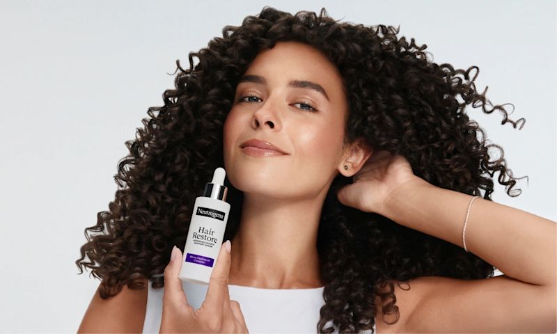 Woman with curly hair holding bottle of Neutrogena® Hair Restore Support Serum