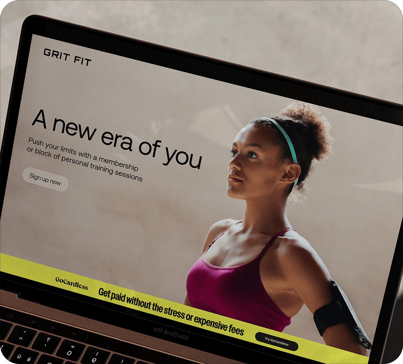 A laptop screen showing a gym website with a woman in gym clothes and the title "A new era of you" with an example of one of the banners from the toolkit at the bottom of the screen that says "Get paid without the stress or expensive fees"