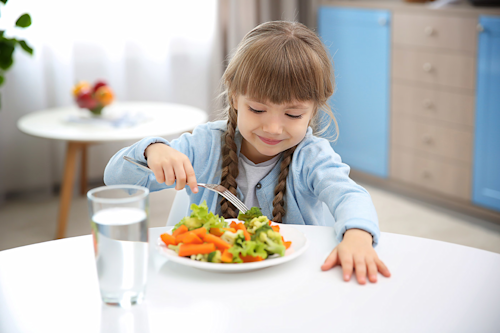 Niña comiendo verduras en un plato durante la comida.