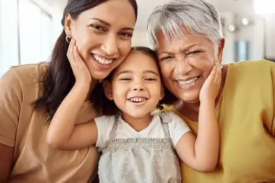 Mujer adulta, niña y adulta mayor sonriendo juntas.
