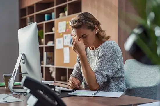 Mujer frente a computadora con cansancio, posible síntoma de anemia.