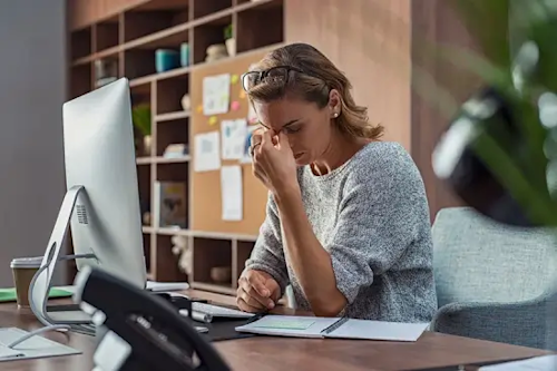 Mujer frente a computadora con cansancio, posible síntoma de anemia.