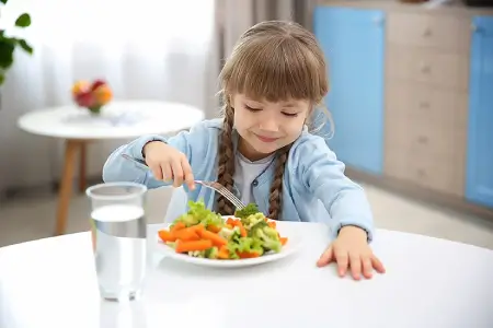 Niña comiendo verduras en un plato durante la comida.