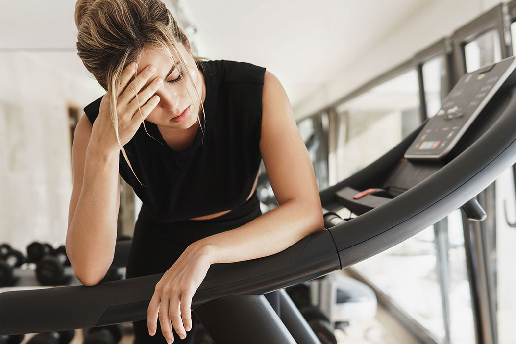 Mujer parada en una cinta de correr cansada con dolor de cabeza