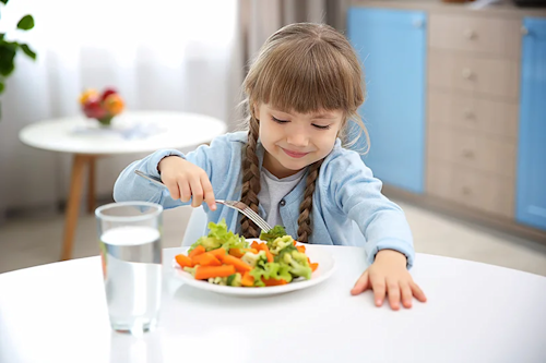 Niña comiendo verduras en un plato durante la comida.