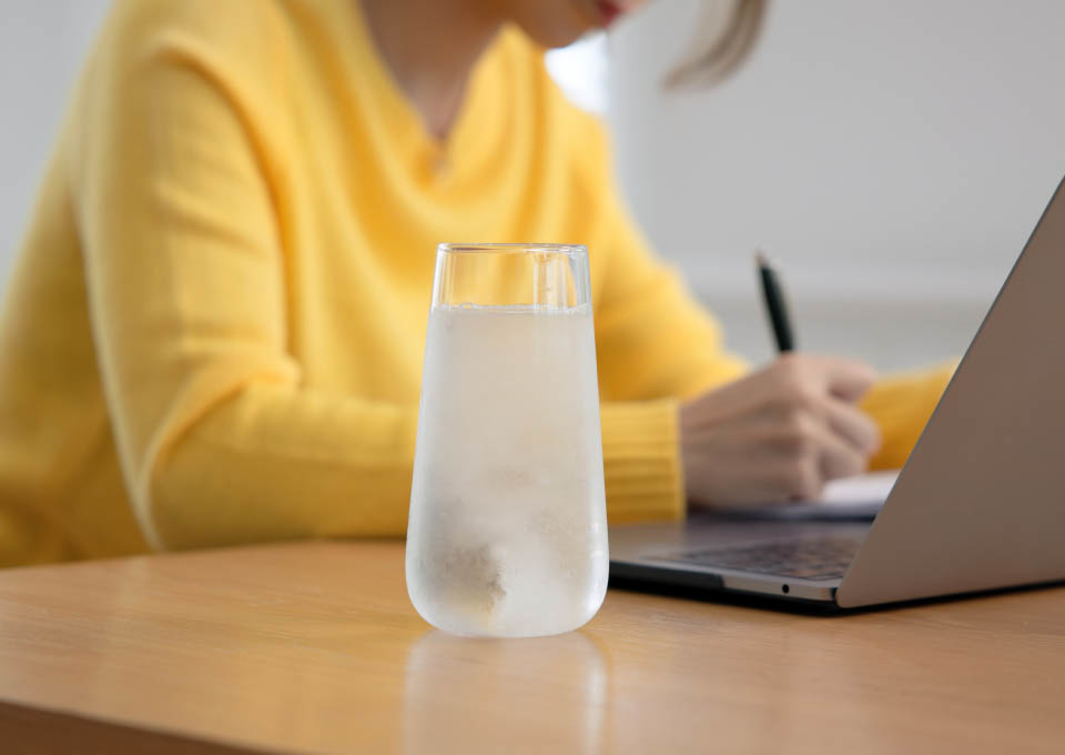 Una mujer trabajando con un ordenador portátil y con un vaso de agua fría a su lado
