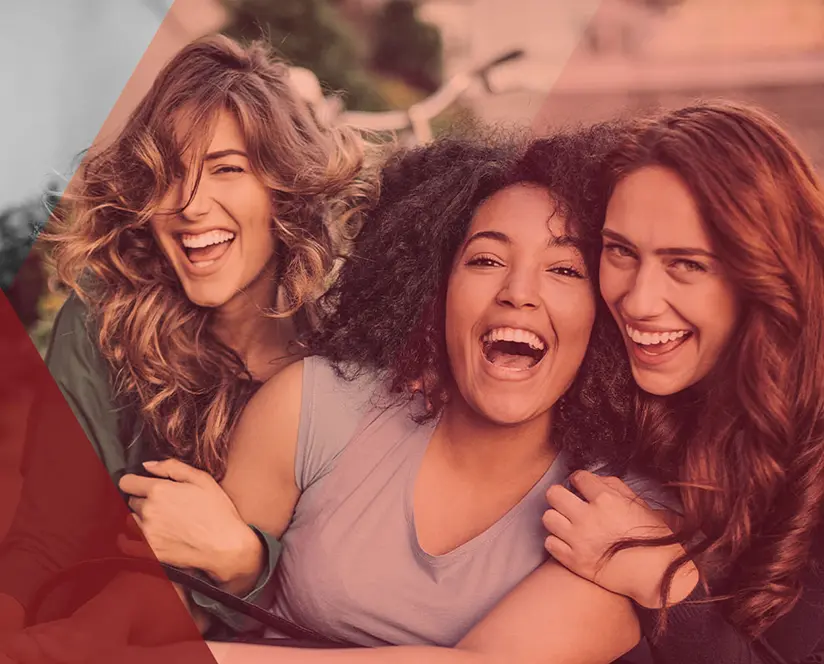 Tres mujeres abrazadas riendo al aire libre.