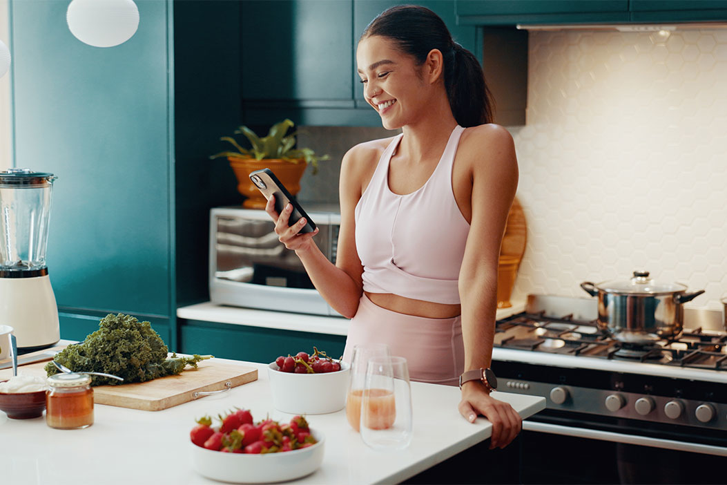 Chica joven con el móvil en la cocina frente a comida saludable rica en hierro