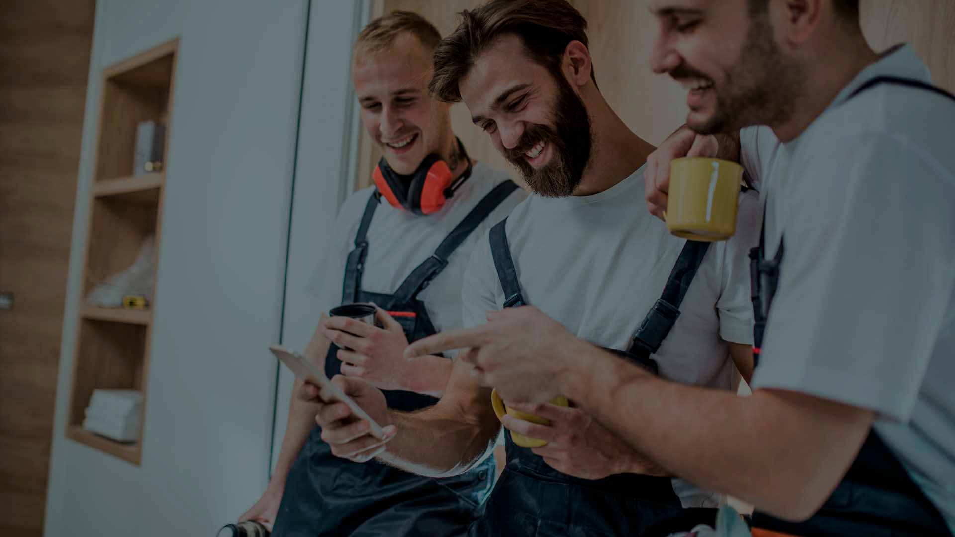 Tre håndværkere med kaffekopper trives med intranet medarbejder app på arbejdspladsen