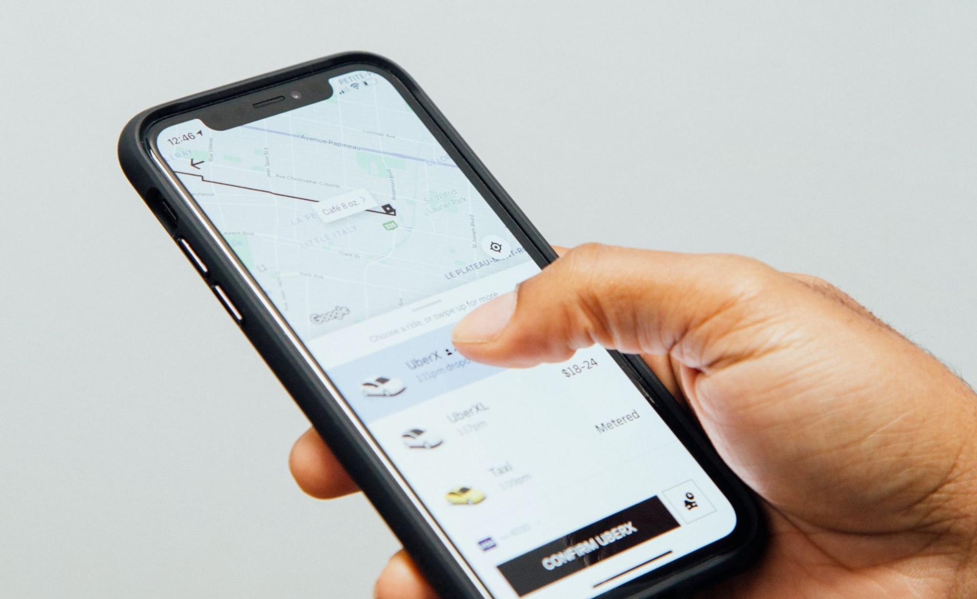 A hand holding a cell phone using the Uber app to choose a driver.