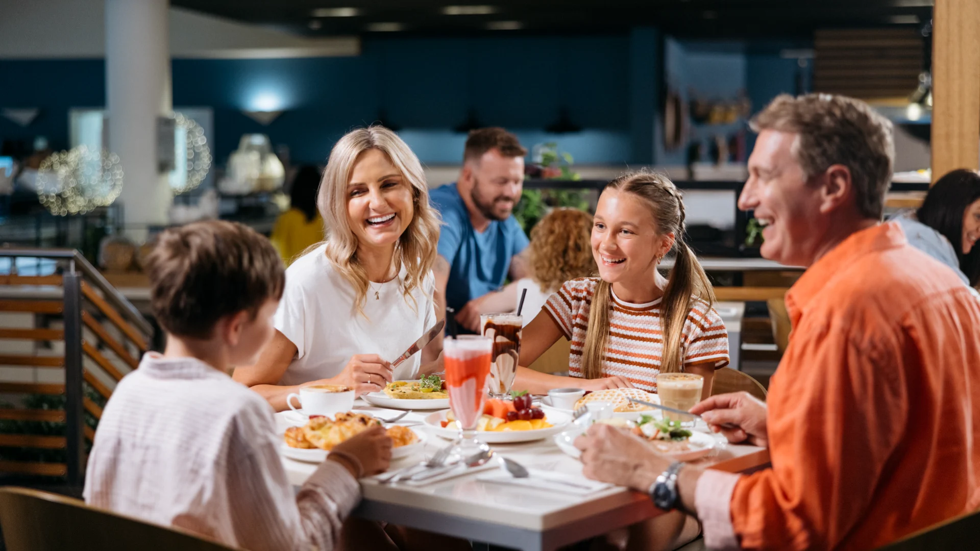 A family of four enjoys a meal together at Shoreline Restaurant, with plates of food and drinks on the table.