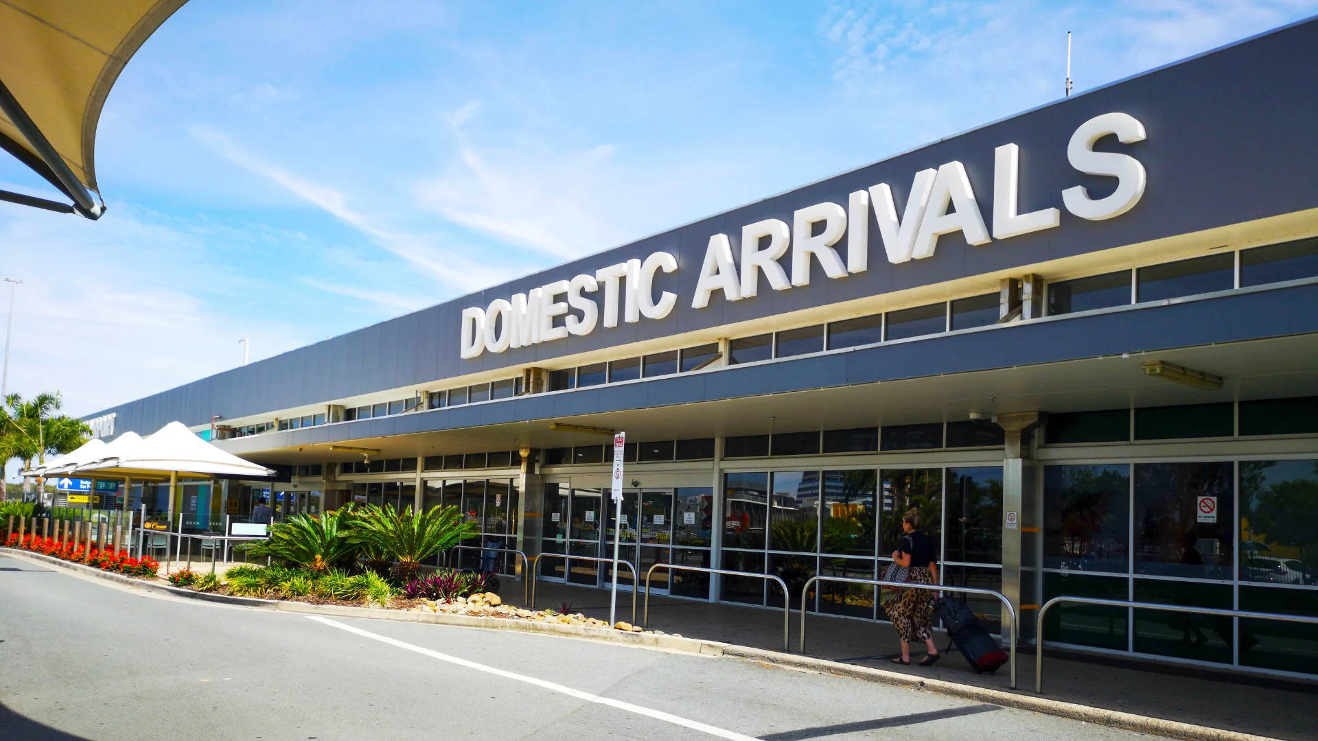 Exterior view of the Domestic Arrivals terminal at the Gold Coast Airport, showing the entrance and a covered walkway.