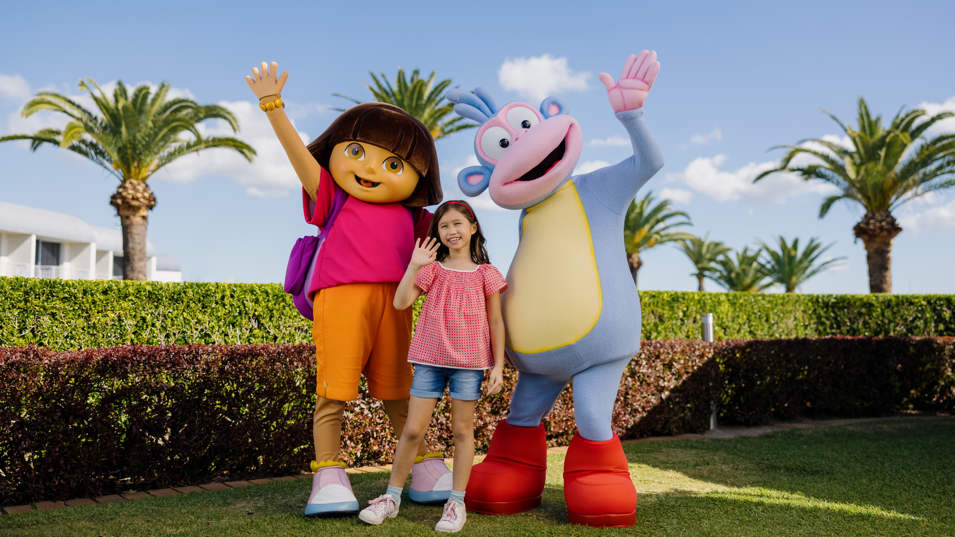 A child posing with Dora the Explorer and Boots on the clear blue sky day.