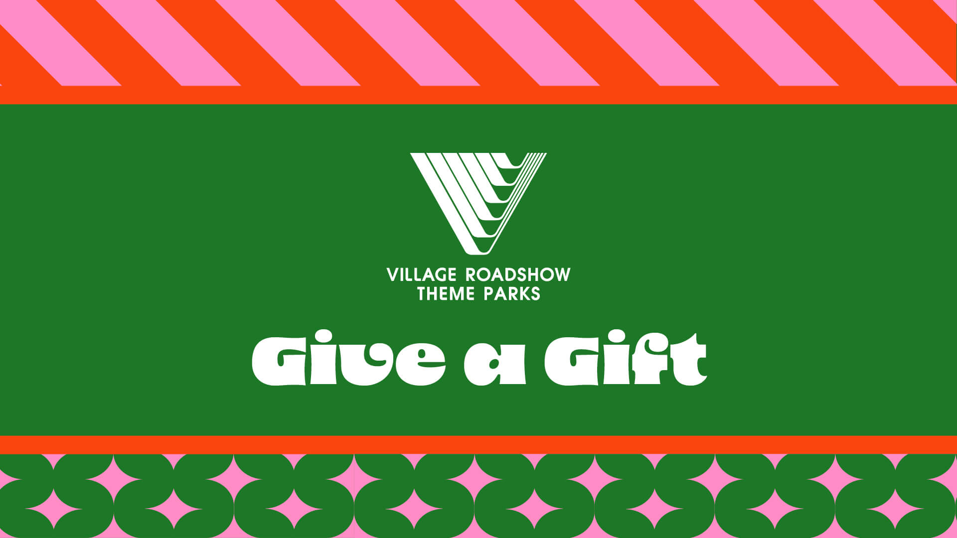 A green card with the Village Roadshow Theme Parks logo, the text "Give a Gift," and decorative pink and red patterns on the top and bottom.