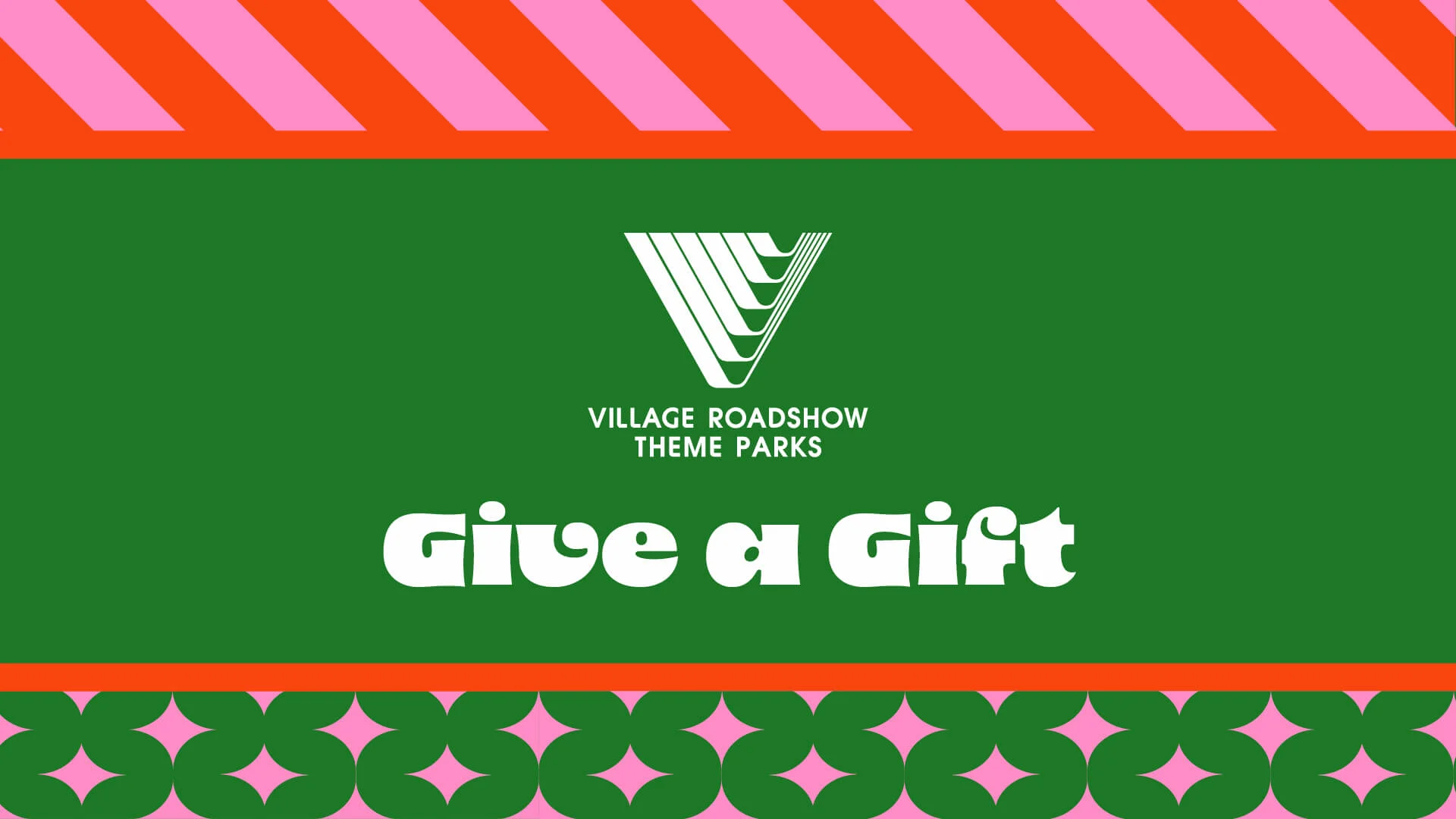 A green card with the Village Roadshow Theme Parks logo, the text "Give a Gift," and decorative pink and red patterns on the top and bottom.
