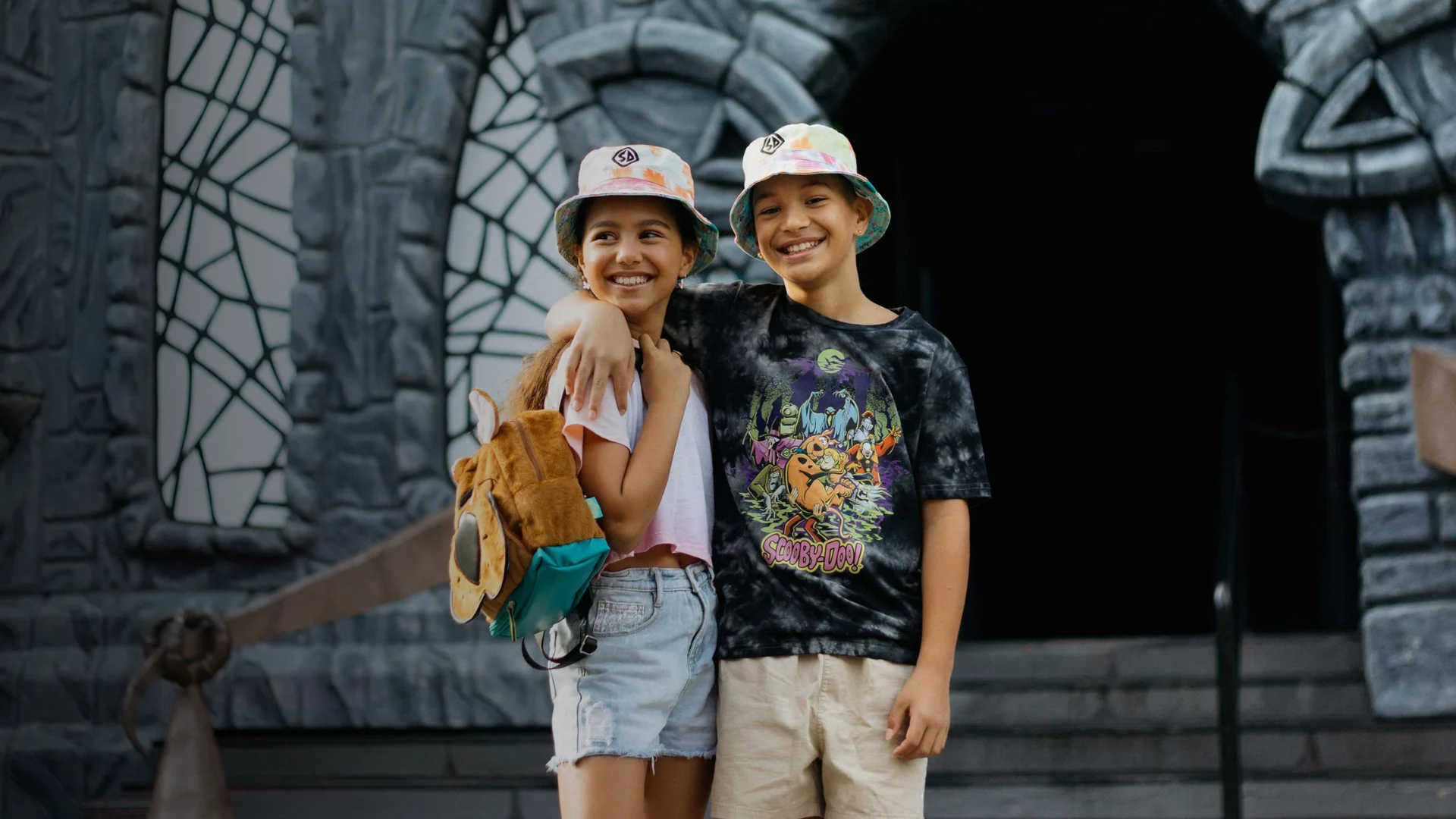 Two kids wearing Scooby-Doo merchandise, posing in front of Scooby-Doo Castle at Warner Bros. Movie World