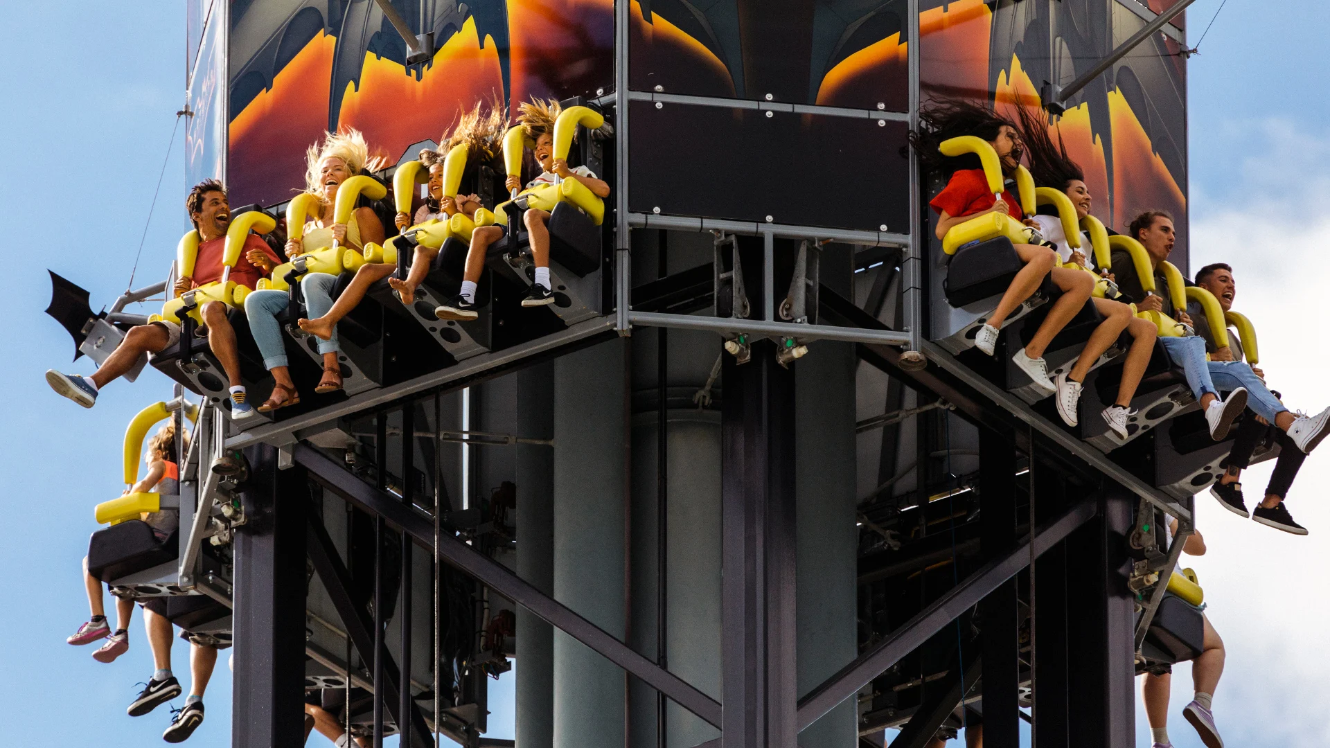Riders experiencing the exhilarating descent on the BATWING Spaceshot ride at Warner Bros. Movie World, with a backdrop of blue sky and the thrill of free-fall excitement