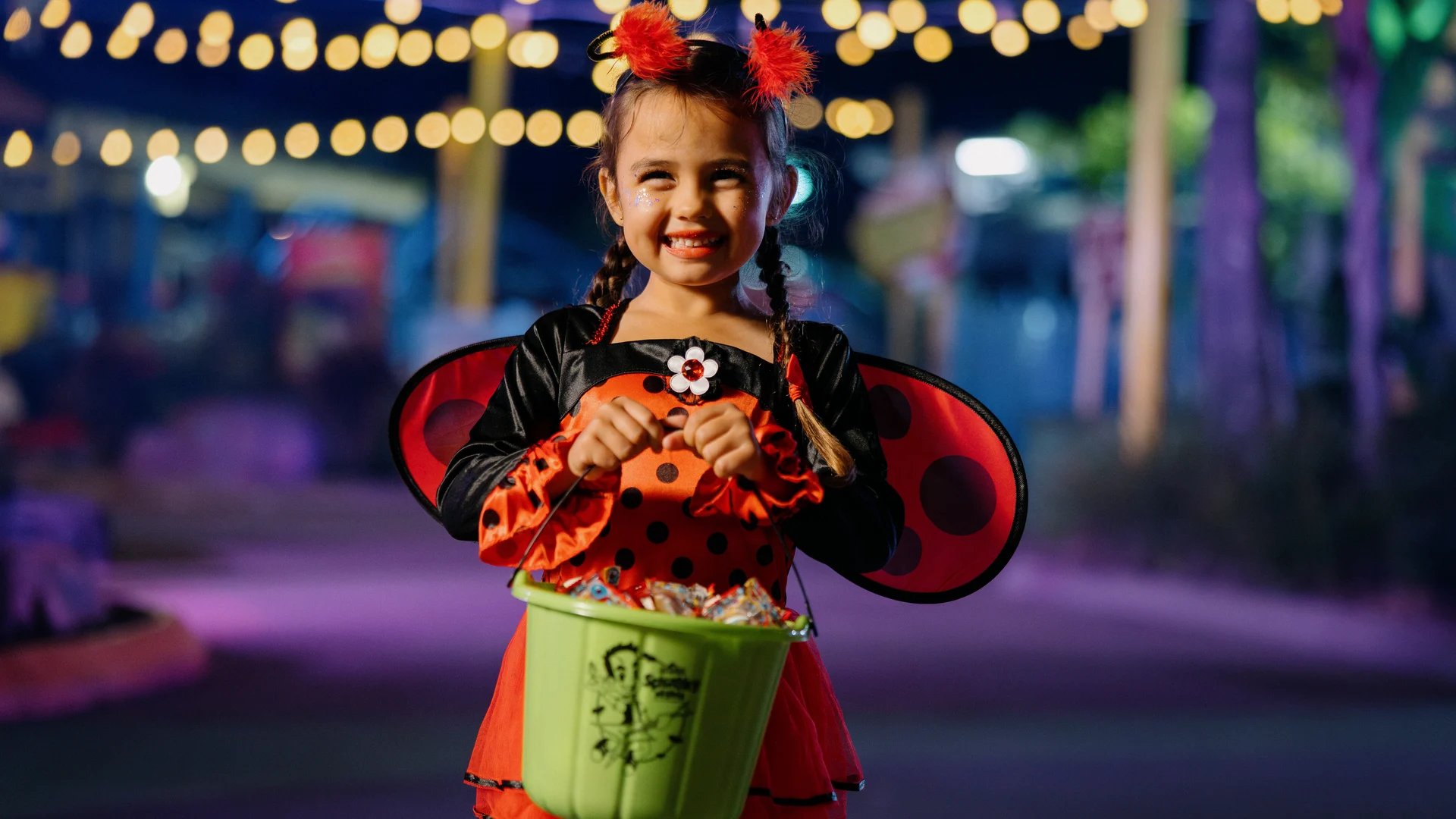 Four children in Halloween costumes excitedly gather around a table filled with candy, holding buckets for trick-or-treating.