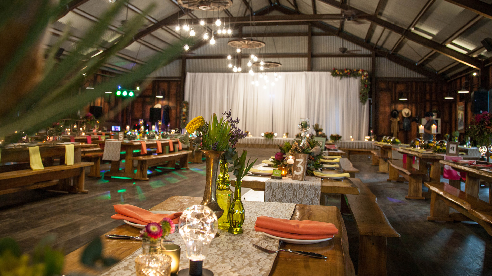 Decorated tables in a rustic restaurant. The tables are decorated with pink napery, Australian native flowers, and candles.