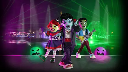 Three colorful, cartoonish monster characters pose on a stage with glowing jack-o'-lanterns and lasers in the background.